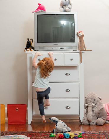 Child climbing on dresser with CRT TV perched on top