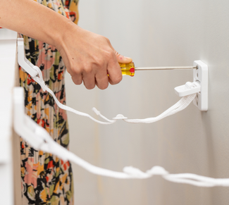 Woman screwing white bracket with straps into drywall