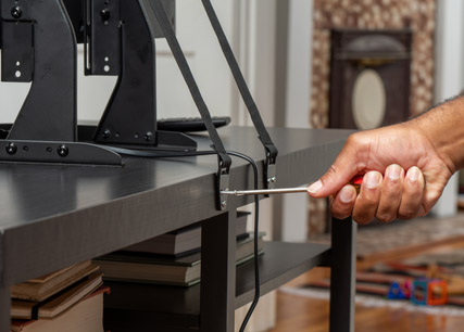 Man screwing brackets into back of TV stand with straps connected to TV